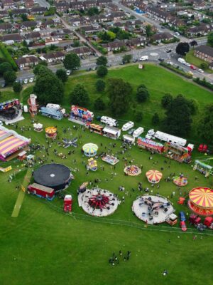 A lively aerial view of an amusement park festival in Luton, England, showcasing rides and green surroundings.